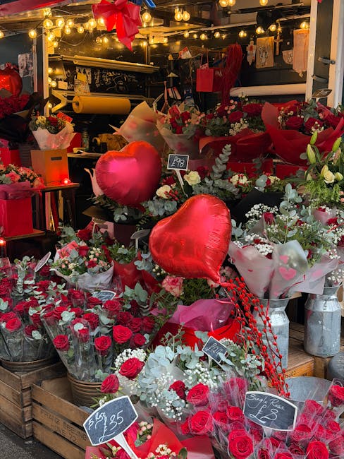 A vibrant display of floral arrangements and bouquets featuring red and white roses, accented with white baby's breath and green foliage, arranged in baskets, vases, and wrapped in pink and red tissue