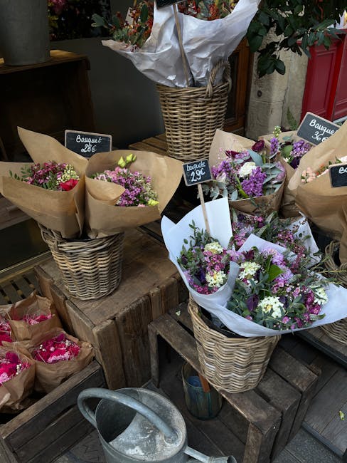 A display of various flower bouquets arranged in woven wicker baskets at a flower shop, featuring pastel-colored flowers including lavender, white, and pink blossoms, wrapped in brown craft paper and 