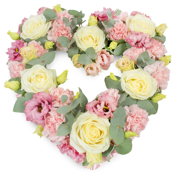 A luxurious heart-shaped floral tribute fills the frame, composed entirely of soft pastel blooms and airy greenery, shown against a bright white backdrop that makes every colour and petal detail stand out. The heart is complete and well-balanced, with no gaps, giving the impression of abundant, unwavering love. Prominent throughout are large, creamy ivory and pale buttery-yellow roses, each one carefully positioned so their swirling centres draw the eye inward, expressing purity, respect, and gratitude. Interlaced with these roses are countless light pink carnations, their intricate ruffles creating a velvety texture across the surface of the heart, like a gentle quilt of petals. Between the carnations and roses, richer magenta-pink to mauve lisianthus blooms appear, some more open, some still cupped, adding graceful variation and a slightly deeper, romantic tone, much like the soft colours seen over the river near Canary Wharf at dusk when viewed from the Isle of Dogs. Silvery eucalyptus, with its smooth, round leaves and muted blue-green hue, winds naturally through the arrangement, offering both structure and a calm, herbal freshness that you can almost imagine breathing in. Tiny, fresh yellowish-green buds punctuate the flowers, small notes of life and continuity that soften the sorrow this tribute is designed to accompany. This heart-shaped wreath carries a quiet yet profound emotional weight, ideal for funeral services, memorial gatherings, or condolence deliveries around Island Gardens, South Quay, or residential streets nearby, where families wish to honour a loved one with a symbol that is both beautiful and deeply sincere, reflecting local floristry skill and careful attention to every stem.